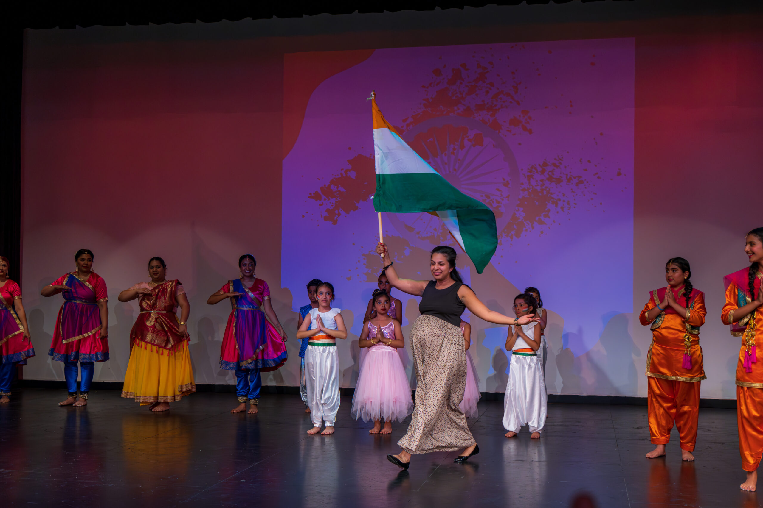 Neha Khanna, founder and artistic director of Dance Expression walking across the stage waving the Indian flag with students in the background.